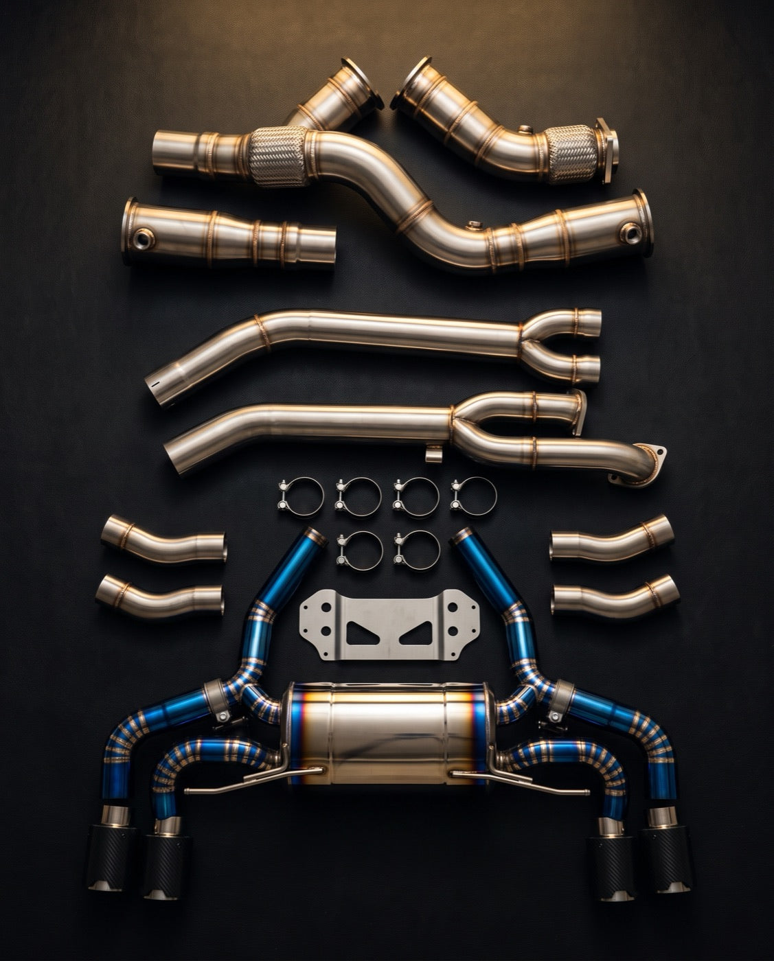 Downpipes, midpipes and a titanium exhaust system laid out on black