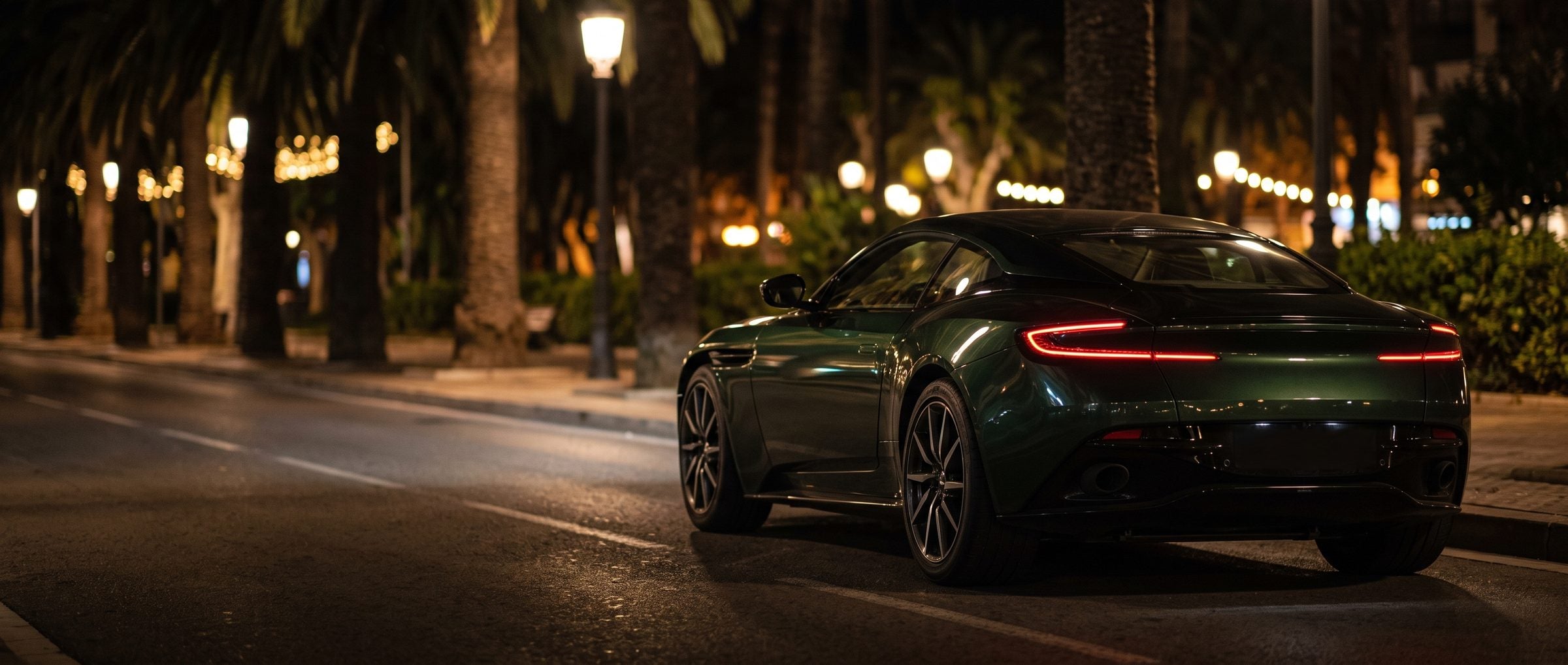 Dark green grand tourer on a palm lined boulevard at night