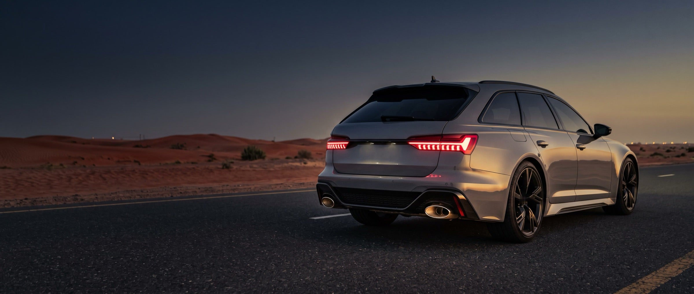Rear of a grey estate car with oval exhaust tips on a desert road at dusk