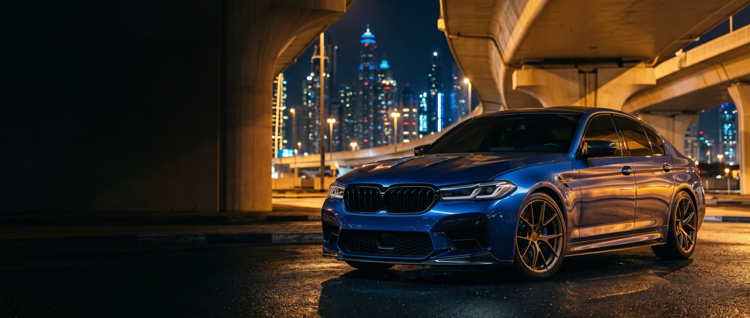 Blue saloon under a highway bridge with a city skyline at night