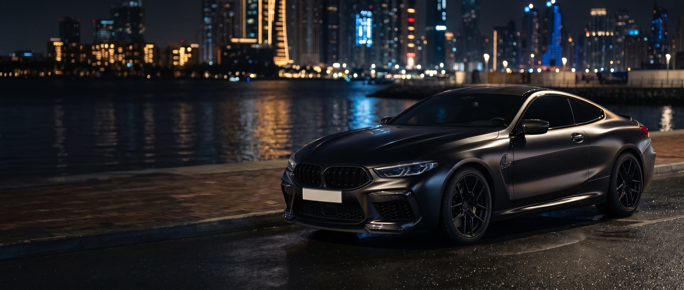 Black coupe by the water with a city skyline at night