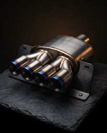 Stainless steel exhaust rear section with four titanium-blue tips on dark slate