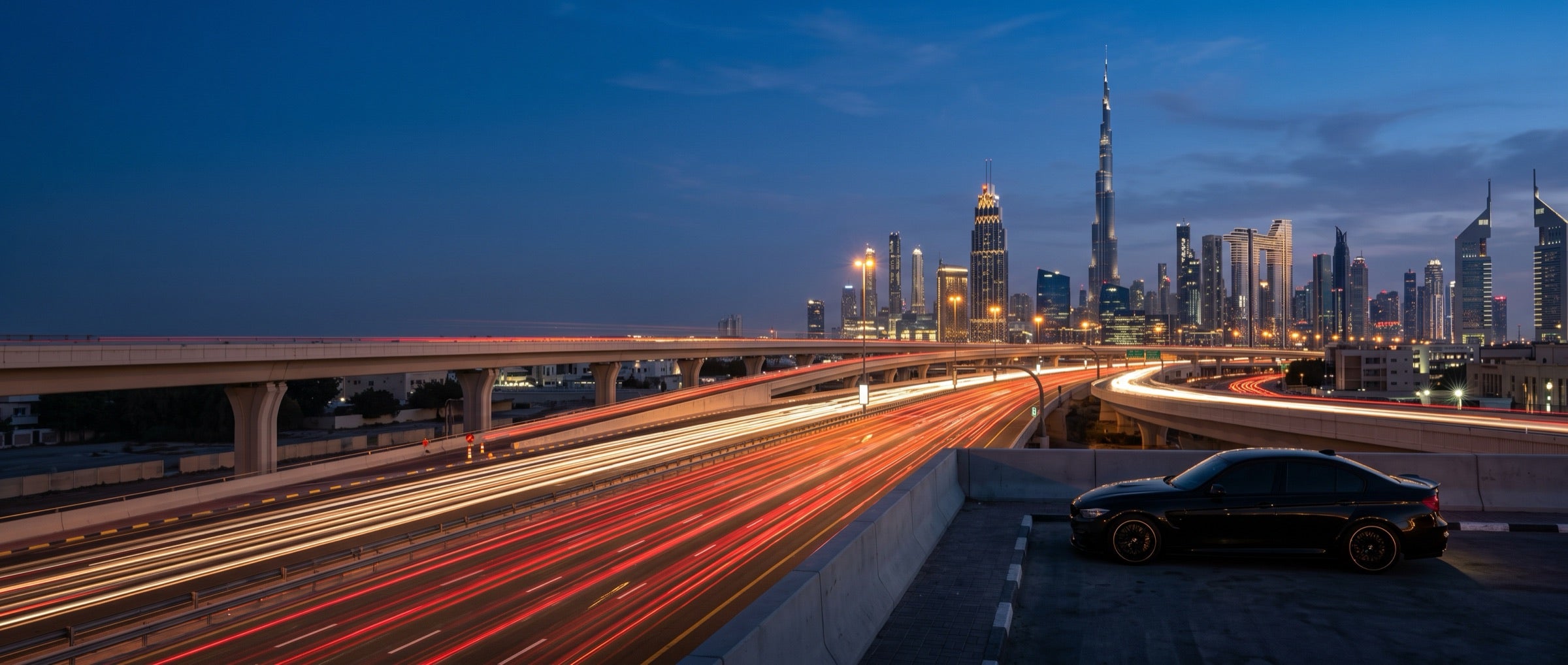 Black saloon parked on a raised road above traffic, with the city skyline at dusk