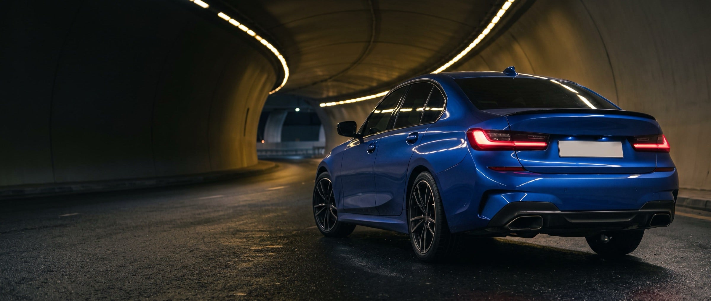 Rear of a blue saloon with twin exhaust tips in a lit tunnel