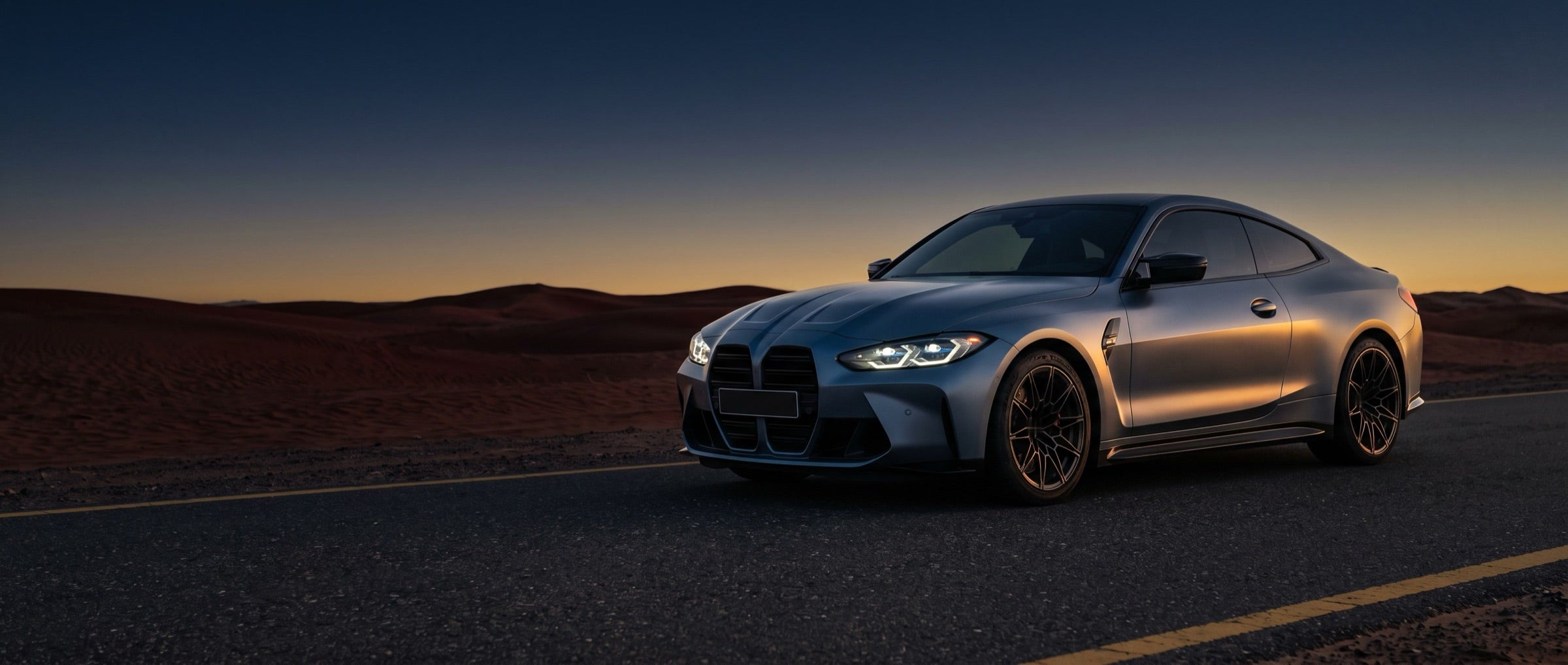 Grey sports coupe on a desert road at dusk