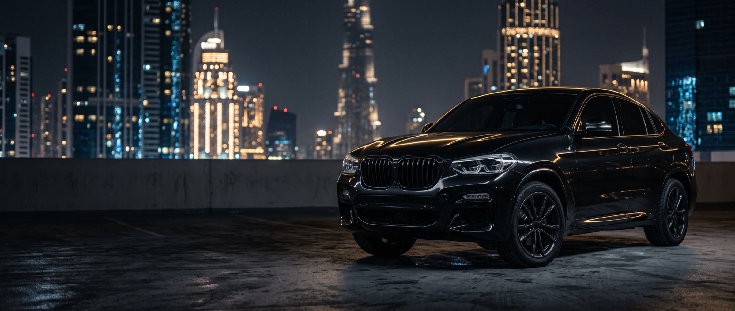 Black coupe SUV on a rooftop car park with a city skyline at night
