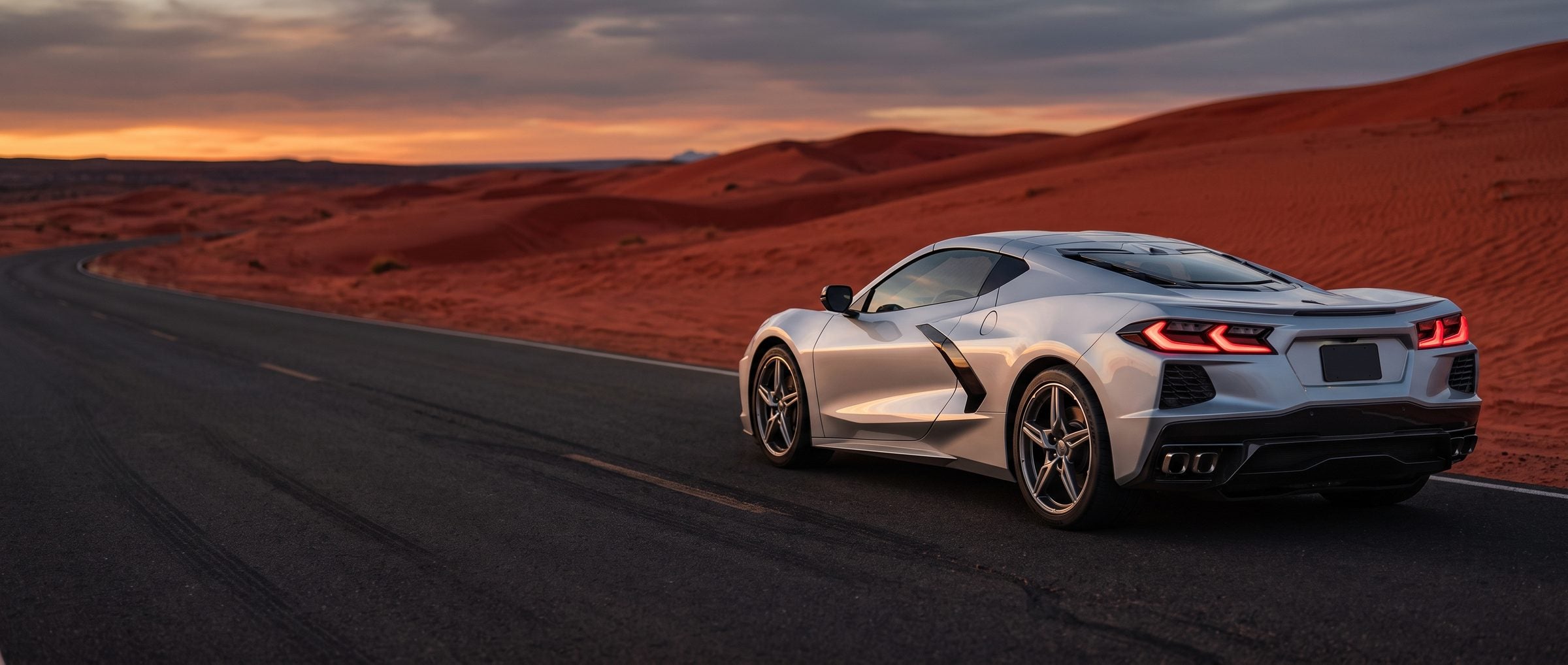Silver mid-engine sports car on a desert highway at dusk