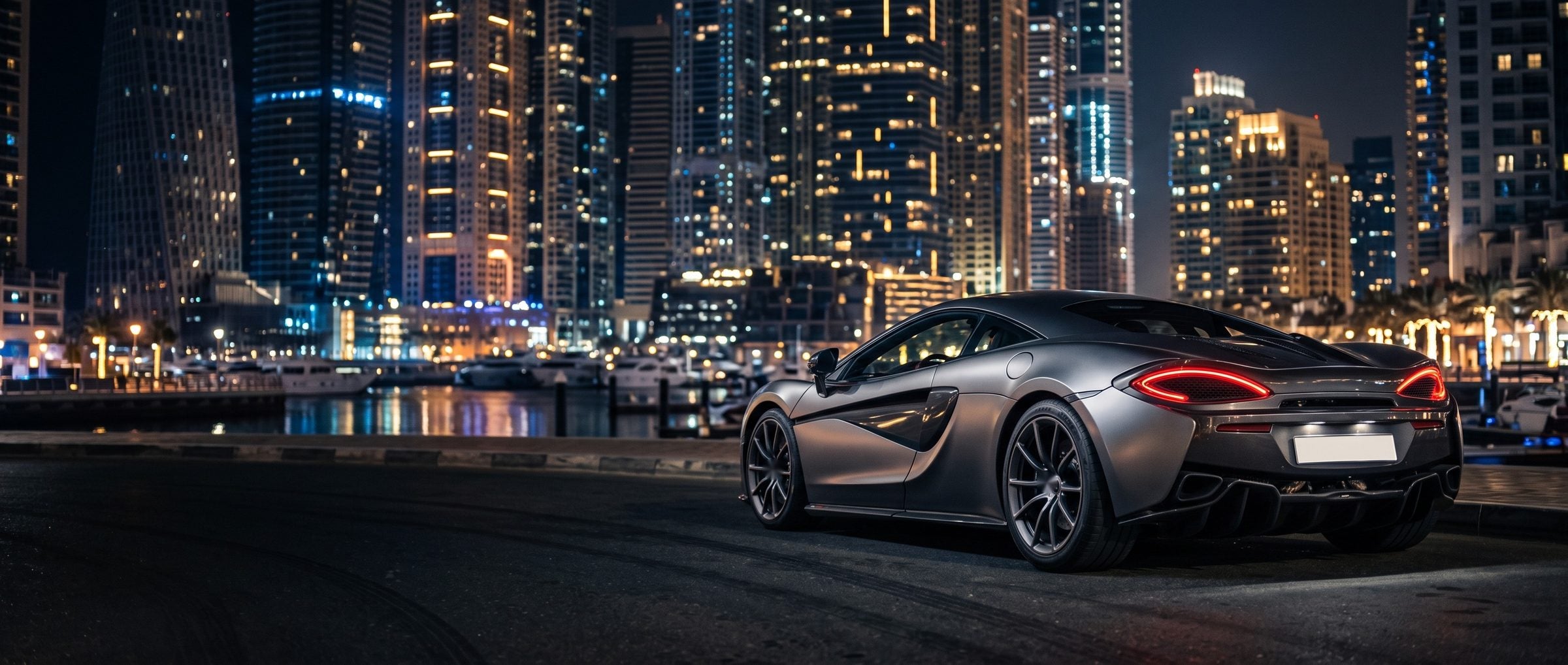 Grey British supercar on a waterfront road at night