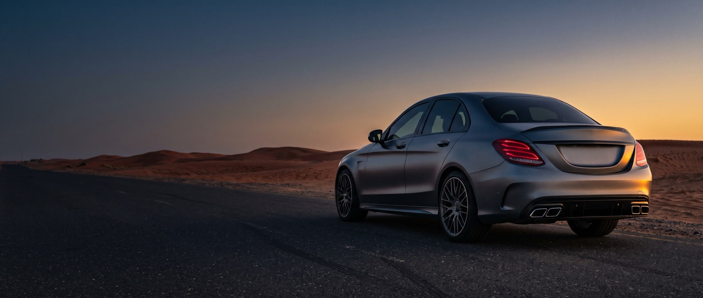 Rear of a grey saloon with quad exhaust tips on a desert road at dusk