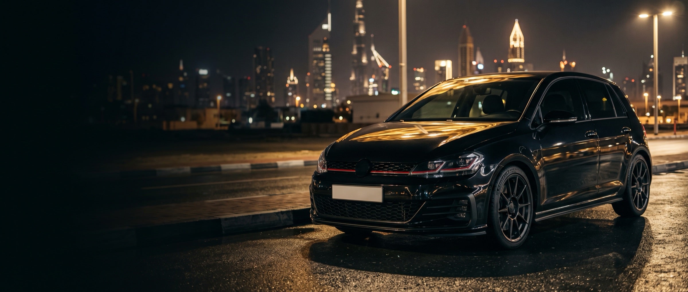 Black hatchback on a wet road with a city skyline at night