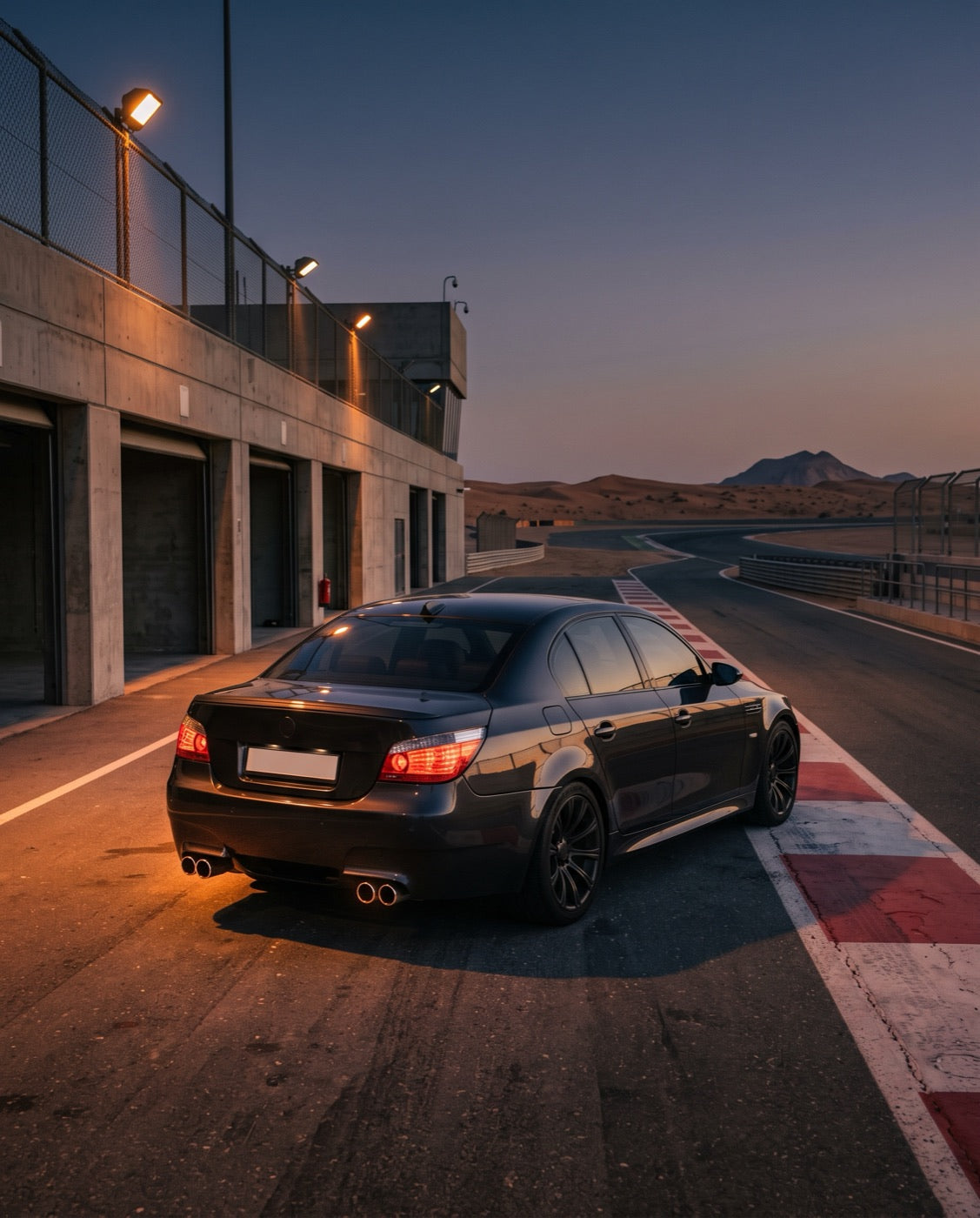 Dark grey saloon at a race circuit pit exit at dusk