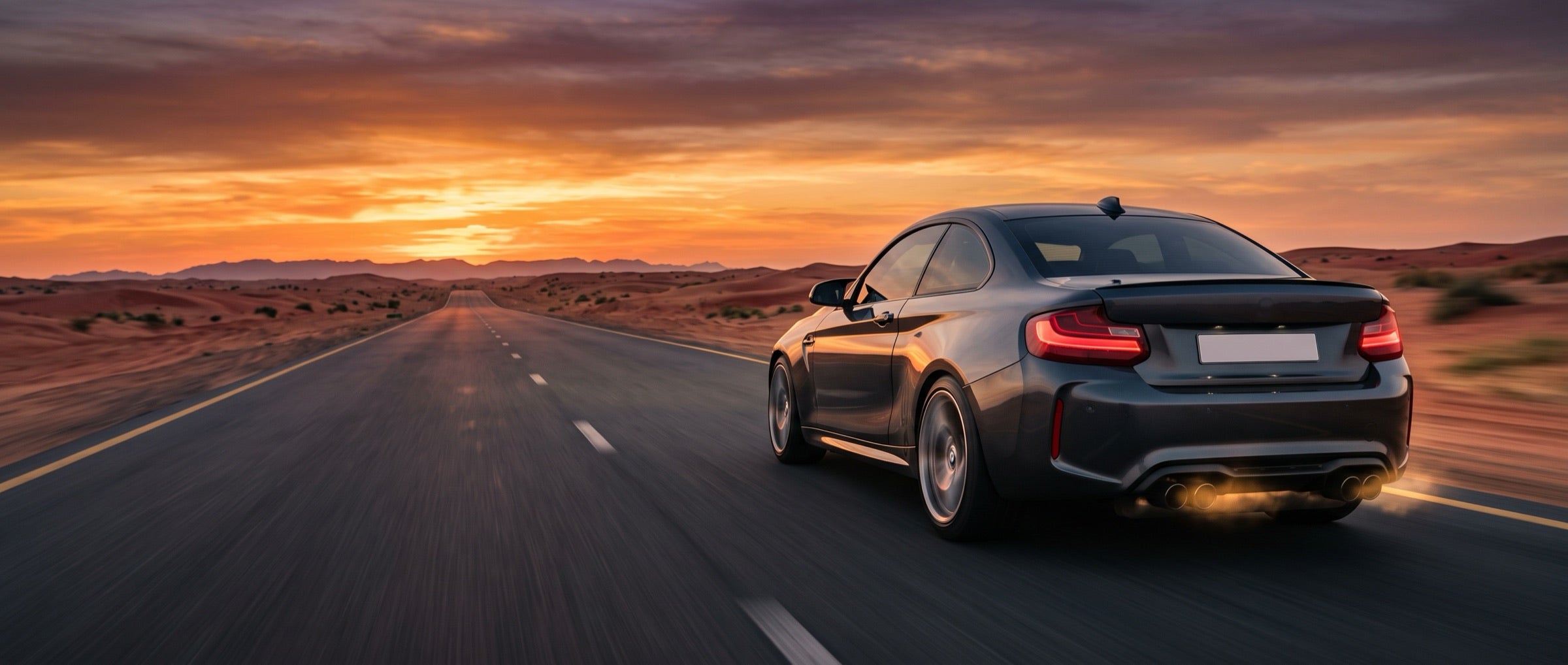Rear of a black coupe on a desert road at sunset