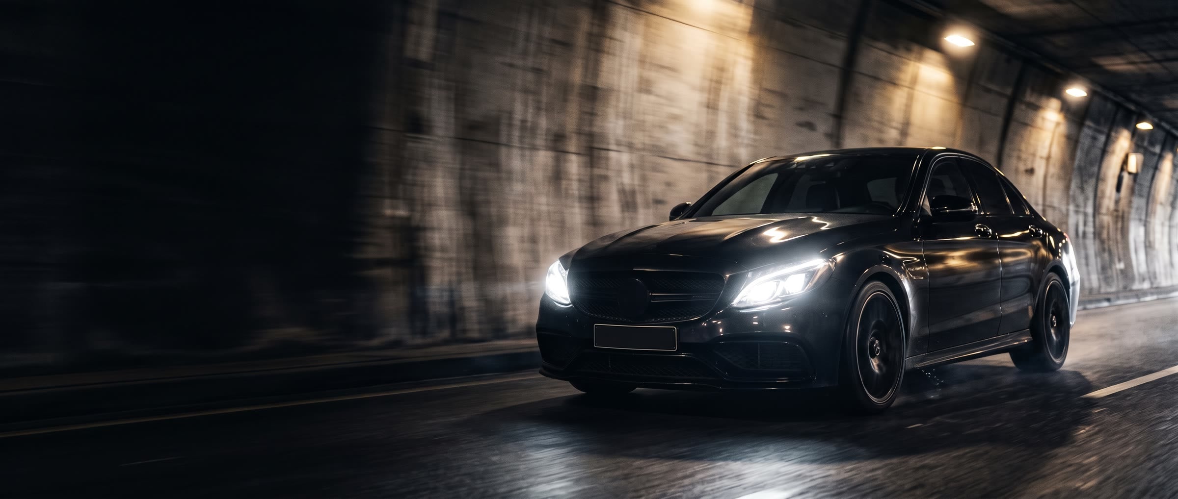 Black saloon driving fast through a lit concrete tunnel at night